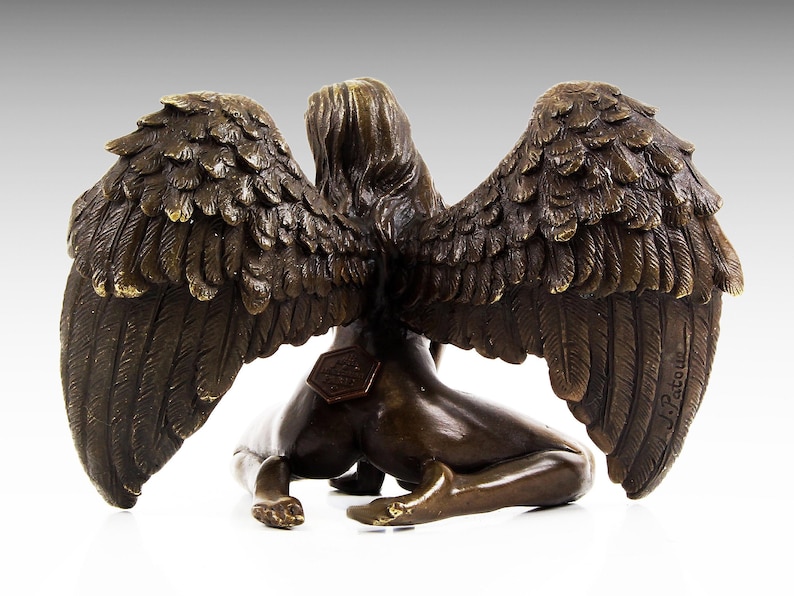 Puede incluir: Escultura de bronce de una figura alada con las alas extendidas. La figura est&aacute; arrodillada con la cabeza girada hacia un lado. La escultura est&aacute; firmada "J. Patou" en el ala derecha.