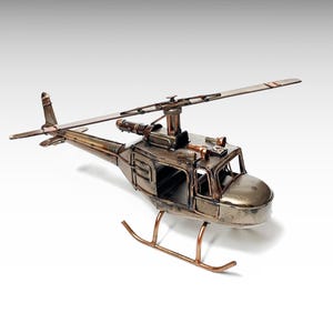 May include: A detailed metal model of a helicopter, featuring a rotor, tail rotor, and landing skids. The model has a metallic finish with copper-colored accents, showcasing intricate details and a vintage aesthetic. The helicopter is positioned against a white background.