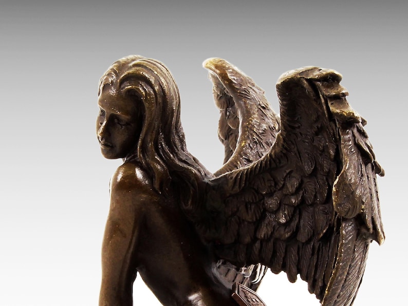 Puede incluir: Escultura de bronce de una mujer con alas. La mujer est&aacute; desnuda y tiene el pelo largo y suelto. Sus alas son grandes y detalladas, con plumas esculpidas en un estilo realista.