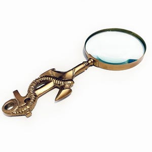May include: A gold-colored magnifying glass with a decorative dragon-shaped handle. The round lens is surrounded by a gold-toned metal rim. The handle features intricate details, including a dragon's head and tail.