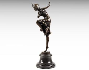 Op de afbeelding: Een donkerbronskleurig beeld van een danser in een dynamische pose, balancerend op één been met uitgestrekte armen. De figuur draagt een hoofdtooi en een rok met ruches, gemonteerd op een ronde, gepolijste zwarte stenen voet met een getrapte vorm.