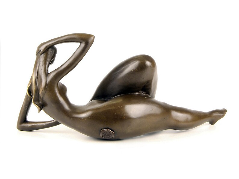 May include: Bronze sculpture of a reclining nude figure. The figure is posed with one arm raised above the head and the other arm resting on the hip. The sculpture is made in a realistic style and has a smooth, polished finish.