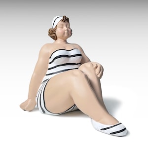Può includere: Statuetta di una donna in costume da bagno a righe bianche e nere e fascia abbinata, seduta con gli occhi chiusi. Indossa scarpe bianche con strisce nere. La statuetta ha la pelle abbronzata e i capelli castani.