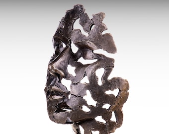 May include: A dark bronze-coloured sculpture depicting a human face in profile. The artwork features a highly textured, weathered surface with numerous irregular cutouts and open spaces, creating a fragmented, abstract appearance throughout the form.