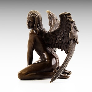 Puede incluir: Una escultura de bronce de un &aacute;ngel arrodillado con alas. El &aacute;ngel est&aacute; desnudo y tiene el pelo largo. Las alas son detalladas y se extienden detr&aacute;s del &aacute;ngel.