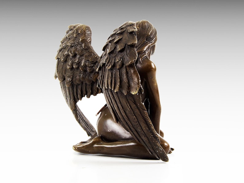 Puede incluir: Una escultura de bronce de un &aacute;ngel con las alas extendidas detr&aacute;s de &eacute;l. El &aacute;ngel est&aacute; arrodillado con la cabeza inclinada. La escultura est&aacute; hecha de bronce marr&oacute;n oscuro y tiene un acabado realista.