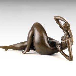 May include: A bronze sculpture of a reclining nude figure. The figure is posed with one arm raised above their head and the other arm resting on their chest. The sculpture is made in a realistic style.