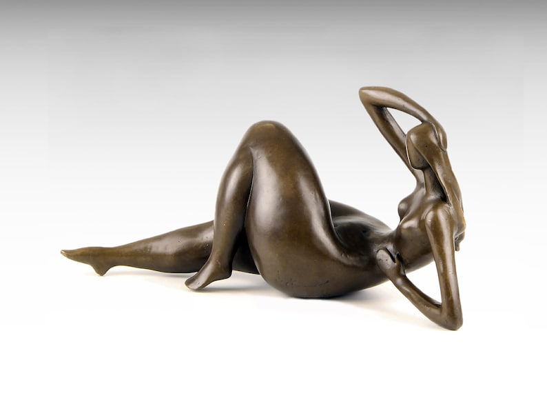 May include: A bronze sculpture of a reclining nude figure. The figure is posed with one arm raised above their head and the other arm resting on their chest. The sculpture is made in a realistic style.