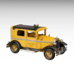 May include: A vintage yellow NYC taxi cab model with a black roof and wheels. The model has the text "N.Y.C TAXI No. 69" on the side and a checkered pattern along the bottom. The taxi has a green light on top.