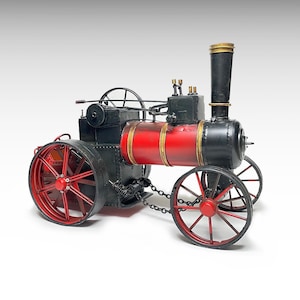 Puede incluir: Modelo detallado de una máquina de vapor vintage. El motor presenta una combinación de colores rojo y negro con detalles dorados. Las ruedas son rojas con llantas negras. El modelo incluye una chimenea y varios componentes mecánicos.