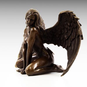 Puede incluir: Escultura de bronce de una mujer con alas. Est&aacute; arrodillada con la cabeza inclinada hacia abajo y las alas extendidas detr&aacute;s de ella.