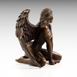 Puede incluir: Escultura de bronce de una mujer arrodillada con alas. La mujer est&aacute; desnuda y tiene el pelo largo. Las alas son detalladas y se extienden detr&aacute;s de ella.