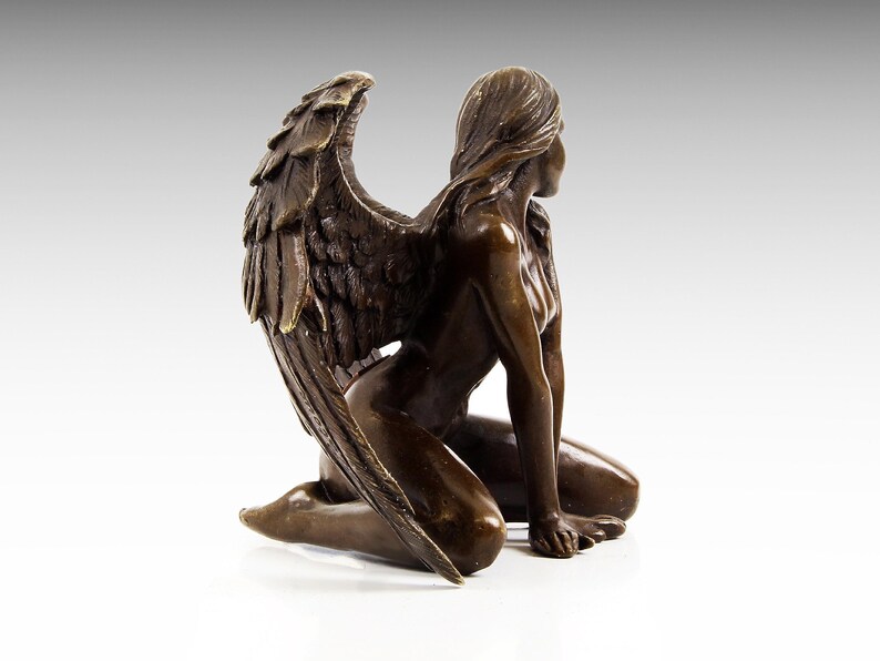 Puede incluir: Escultura de bronce de una mujer arrodillada con alas. La mujer est&aacute; desnuda y tiene el pelo largo. Las alas son detalladas y se extienden detr&aacute;s de ella.