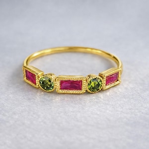 May include: A gold ring with alternating red rectangular and green round gemstones. The ring's design features a thin gold band. The gemstones are set in a decorative gold setting.