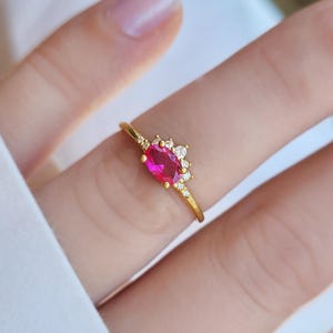 Peut inclure: Une bague en or ornée d'un rubis ovale rouge vif en son centre. La bague est ornée de petits diamants transparents et possède un anneau fin. La bague est un bijou.