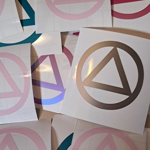 May include: A collection of stickers featuring a circle with a triangle inside. The stickers are in various colors, including teal, pink, red, purple, and gold.