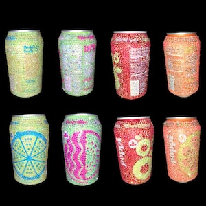 May include: An assortment of eight soda cans, each covered in colorful rhinestones. The cans feature various designs, including a lime slice, a pink and green pattern, and the word "Poppi". Colors include green, pink, orange, and red.