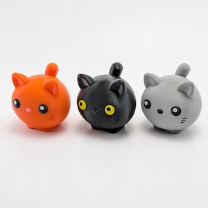 May include: Three small plush cat toys. The cat on the left is orange, the cat in the middle is black with yellow eyes, and the cat on the right is gray.