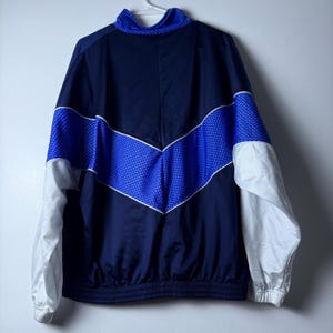 Może przedstawiać: Niebieska i biała kurtka treningowa z białym zamkiem błyskawicznym i niebiesko-białym wzorem w chevron na przodzie.