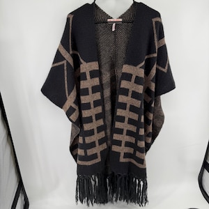 Peut inclure: Un poncho en tricot noir et beige avec un motif géométrique de barres verticales et horizontales. Le vêtement présente une ouverture sur le devant, une étiquette au col indiquant GIL BARET et des franges le long de l'ourlet inférieur.