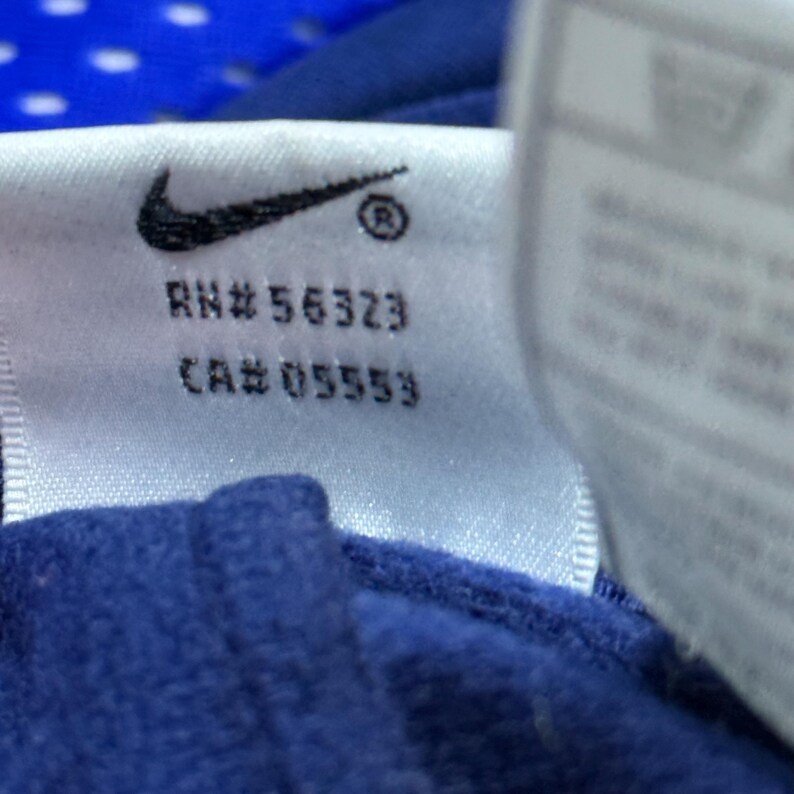Może przedstawiać: Biała metka z czarnym logo Nike swoosh i tekstem "RN# 56323 CA# 05553".