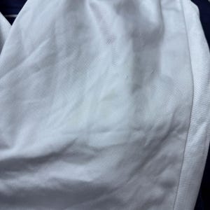 Może przedstawiać: Biały materiał z lekkim odbarwieniem. Materiał ma gładką fakturę i subtelny połysk.