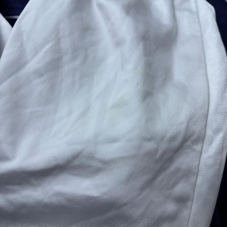 Może przedstawiać: Biały materiał z lekkim odbarwieniem. Materiał ma gładką fakturę i subtelny połysk.