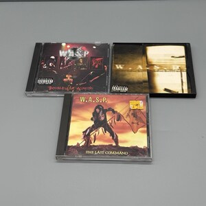 May include: Three W.A.S.P. music CDs. The top left CD is titled "Double Live Assassins" with a live performance photo. The top right CD is a black case with the band's name. The bottom CD is "The Last Command" with a warrior graphic.