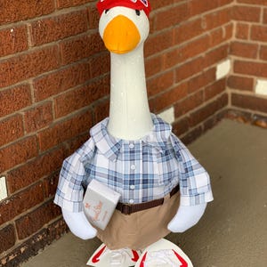 May include: A white goose wearing a red baseball cap with the text "Bubba Gump Shrimp Co." and a blue and white plaid shirt. The goose is holding a small white box with the text "Russell Stover" and is wearing brown pants and white sneakers.