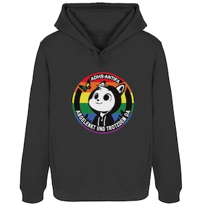 Könnte beinhalten: Schwarzer Kapuzenpullover mit einem kreisförmigen Aufdruck. Der Aufdruck enthält eine Cartoonfigur, einen Regenbogen und den Text "ADHS-ANTIFA ABGELENKT UND TROTZDEM DA". Ein Schmetterling ist ebenfalls im Design enthalten.