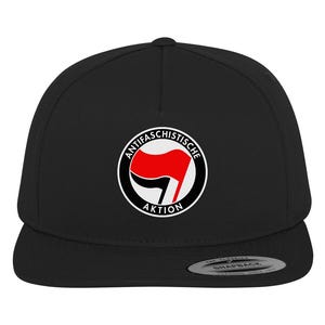 Może przedstawiać: Czarna i biała czapka z daszkiem z czerwono-białym symbolem antyfaszystowskim i tekstem "Antifachistische Aktion".