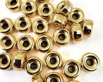 May include: A group of 20 gold-colored metal beads with a hole in the center. The beads are round and have a raised edge around the hole. The beads are scattered on a white surface.