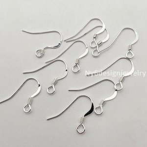 May include: A collection of silver-colored earring hooks. The hooks are curved with a looped bottom and a coiled wire detail. The hooks are designed for jewelry making and are displayed against a light background.