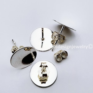May include: Silver-colored earring posts and backs. The posts have a flat, round base with a post extending from the center. The backs are butterfly style. The image is on a white background.