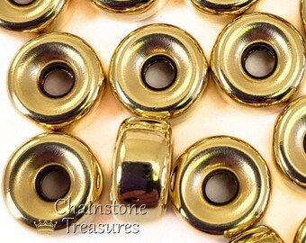 May include: Close-up of multiple gold-colored metal beads with a shiny finish. The beads are round with a central hole and a flat, circular design. The text "Chainstone Treasures" is visible on one of the beads.