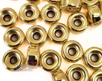 May include: A group of gold-colored metal beads with a raised center and a hole in the center. The beads are arranged in a random pattern on a white surface.