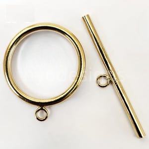 May include: A gold-colored toggle clasp set, featuring a circular ring and a straight bar with a small loop. The clasp is designed for jewelry making and has a shiny, metallic finish.