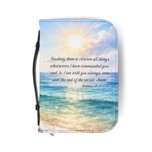May include: A Bible cover featuring a serene ocean scene with a bright sun and text from Matthew 28:20 KJV. The cover has a black handle and a zipper closure. The design includes blue, white, and yellow hues.