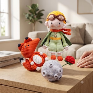 Peut inclure: Un ensemble de trois figurines au crochet comprenant une petite personne aux cheveux jaunes, lunettes marron, cape verte et bottes orange, un renard orange vif aux oreilles et queue à pointes noires, et une planète grise cratérisée avec une rose rouge.