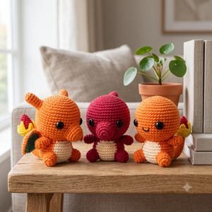 Peut inclure: Trois peluches crochetées comprenant deux créatures orange ressemblant à des dragons avec un ventre crème et une queue enflammée, et une créature centrale rouge foncé avec un ventre crème, toutes avec des yeux en perles noires.