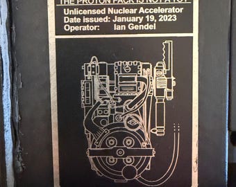 Puede incluir: Una etiqueta de advertencia rectangular negra con texto plateado y un dibujo lineal de un paquete de protones. El texto dice: WARNING THE PROTON PACK IS NOT A TOY Unlicensed Nuclear Accelerator Date issued: January 19, 2023 Operator: Ian Gendel.