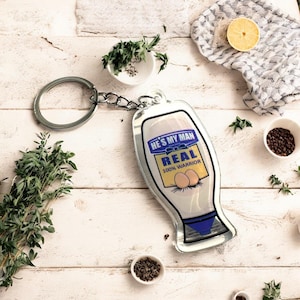 May include: Silver keyring shaped like a mayonnaise bottle with the text "He's my man, Real 100% Warrior" and two eggs on the front.