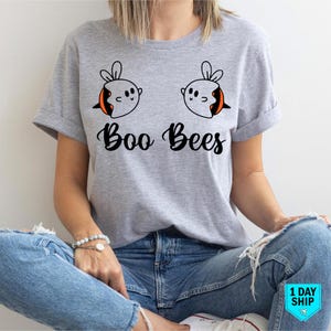 May include: A light grey t-shirt with a fun design of two cartoon bees and the words "Boo Bees" in a script font. The bees have orange and black details. The shirt is worn with blue jeans.