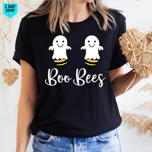 May include: Black t-shirt with a graphic of two white ghost-bee hybrids with yellow and black stripes. The words "Boo Bees" are written in white script below. A casual style shirt, suitable for Halloween or themed events.