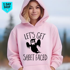 May include: A pale pink hoodie featuring the phrase "LET'S GET SHEET FACED" and a black ghost illustration. The sweatshirt has a hood with a drawstring and long sleeves. A "1 DAY SHIP" graphic is in the upper left corner.