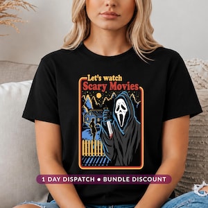 May include: A black short-sleeved t-shirt featuring a graphic print of a hooded figure holding a knife. The text "Let's watch Scary Movies" appears above the illustration, which depicts a house, a silhouette, and a fence under a night sky.