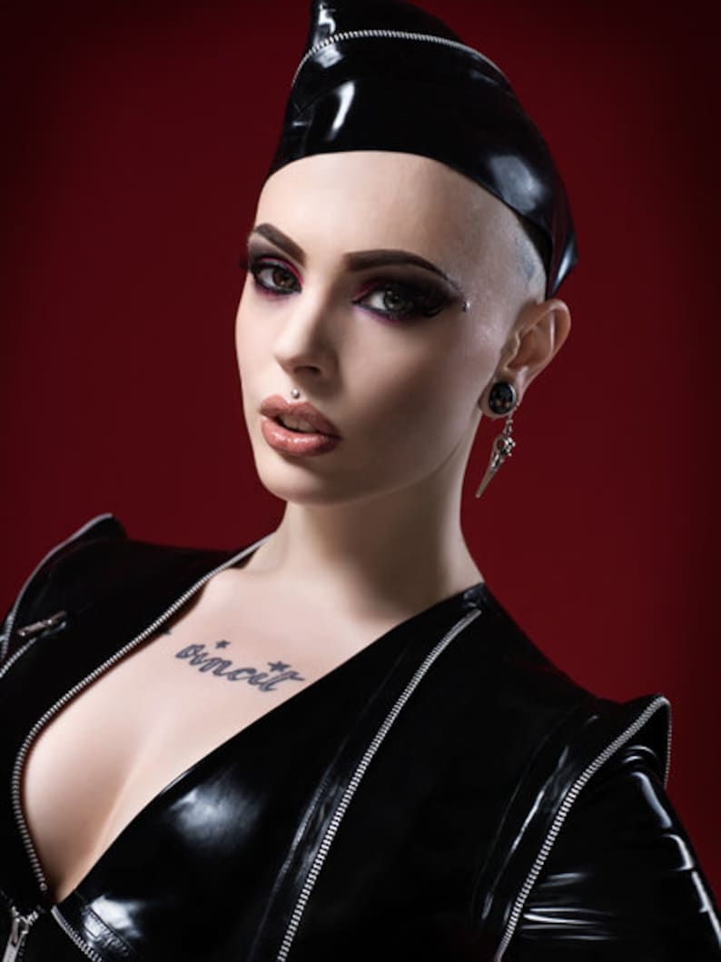 May include: A woman wearing a black leather jacket with a zipper detail and a black leather cap. She has a tattoo on her chest that says "binecuit".