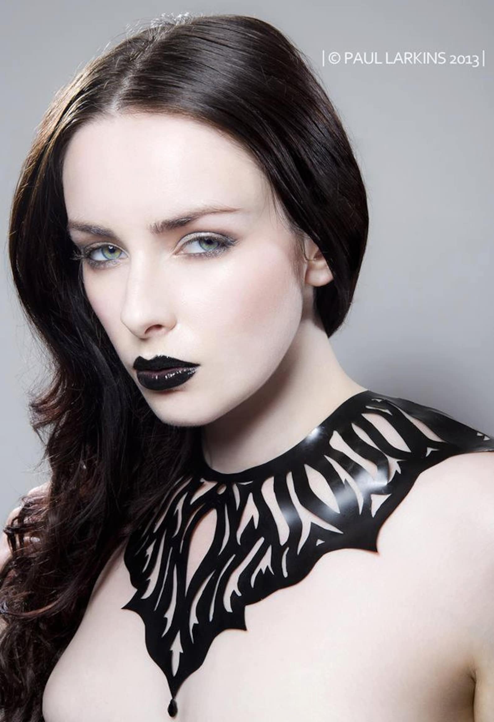 Side view of high-fashion latex choker with organic cutouts and glossy black finish on pale model.