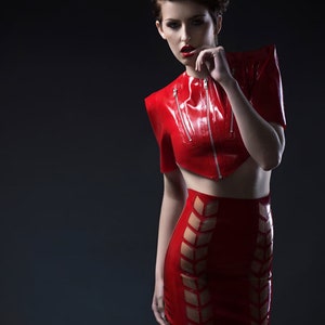 Pu&ograve; includere: Una donna indossa un top e una gonna in lattice rosso con un design geometrico. Il top ha una cerniera e la gonna ha un'alta vita.