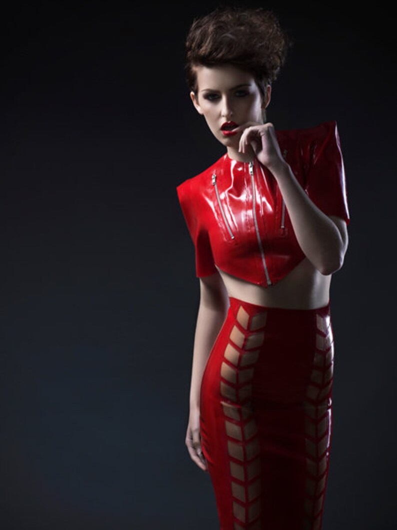Pu&ograve; includere: Una donna indossa un top e una gonna in lattice rosso con un design geometrico. Il top ha una cerniera e la gonna ha un'alta vita.